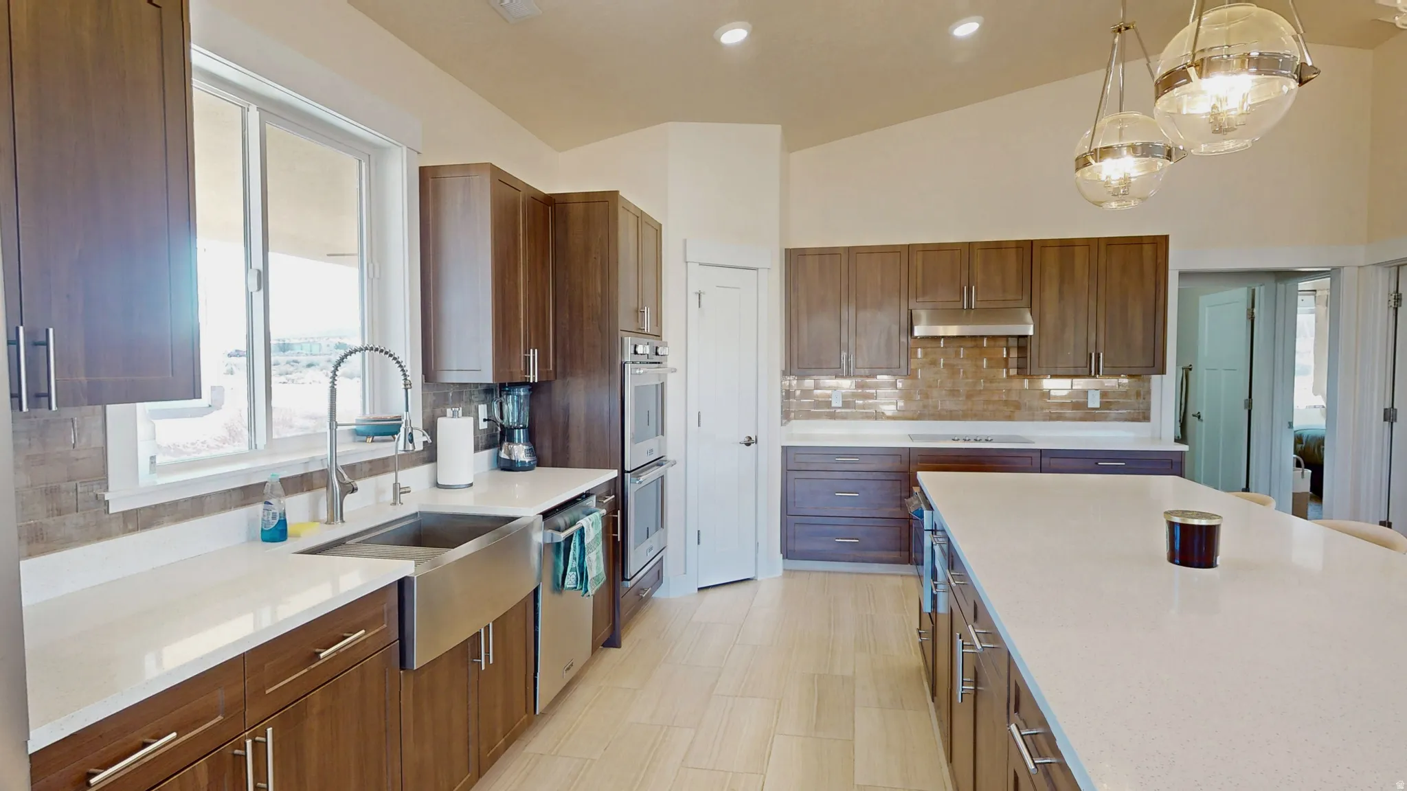 Kitchen featuring brown cabinetry, light stone counters, pendant lighting, lofted ceiling, and stainless steel appliances