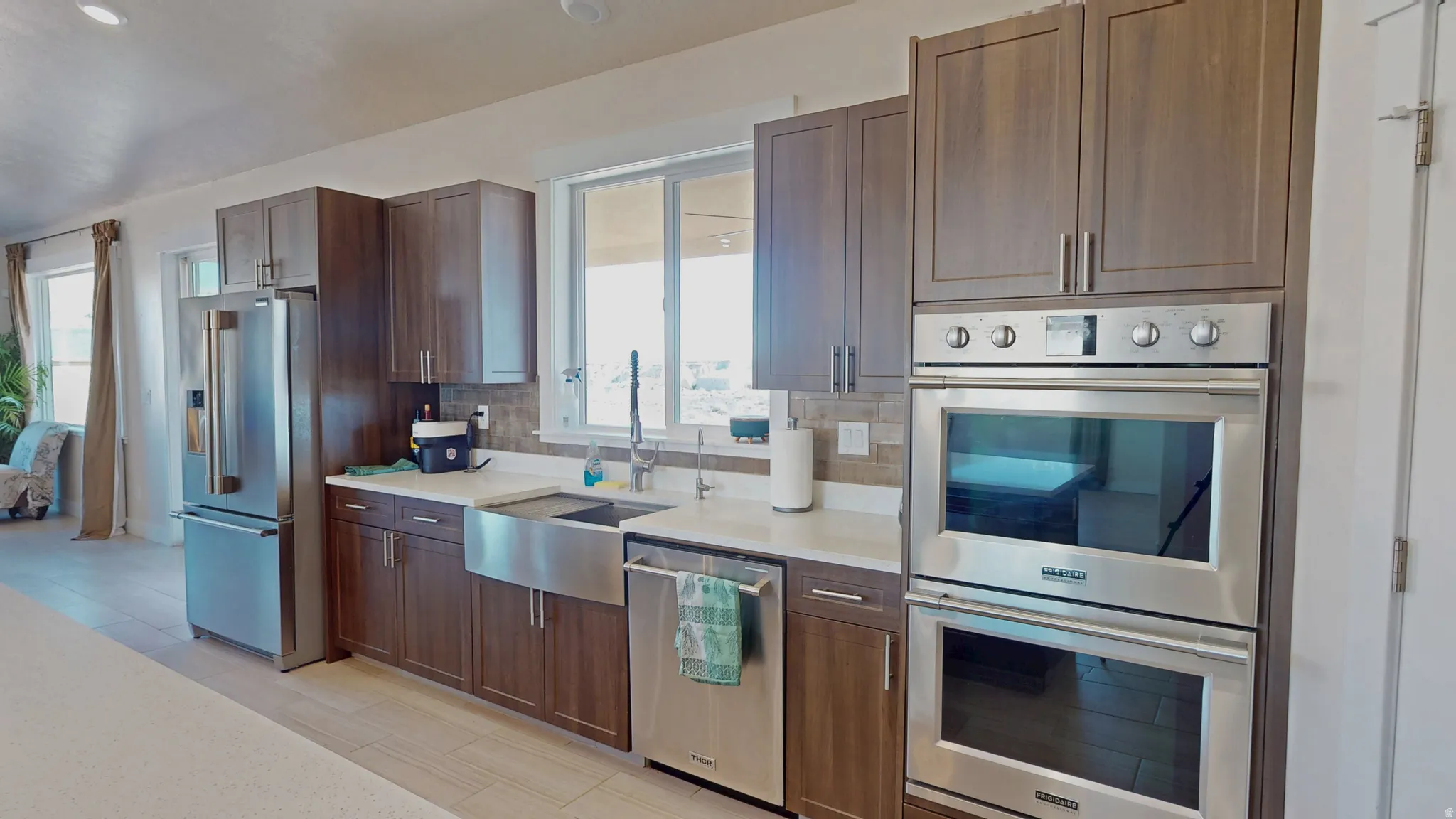Kitchen featuring appliances with stainless steel finishes, decorative backsplash, dark brown cabinetry, and light stone countertops