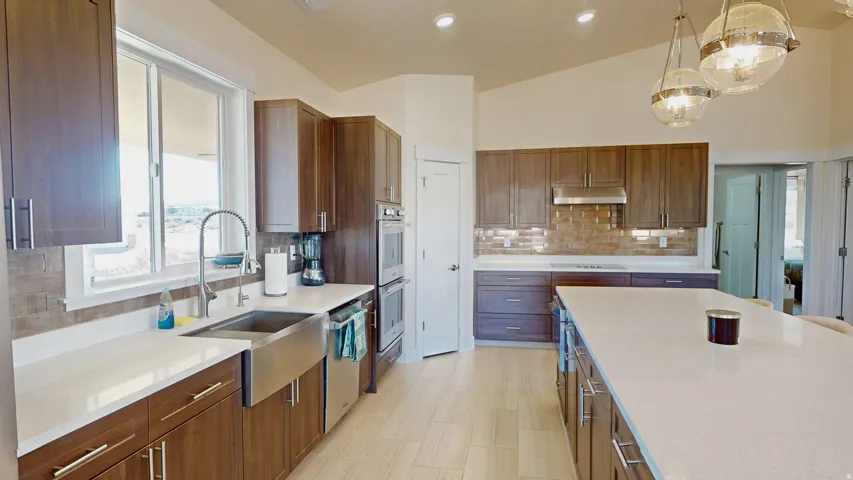 Kitchen featuring brown cabinetry, light stone counters, pendant lighting, lofted ceiling, and stainless steel appliances