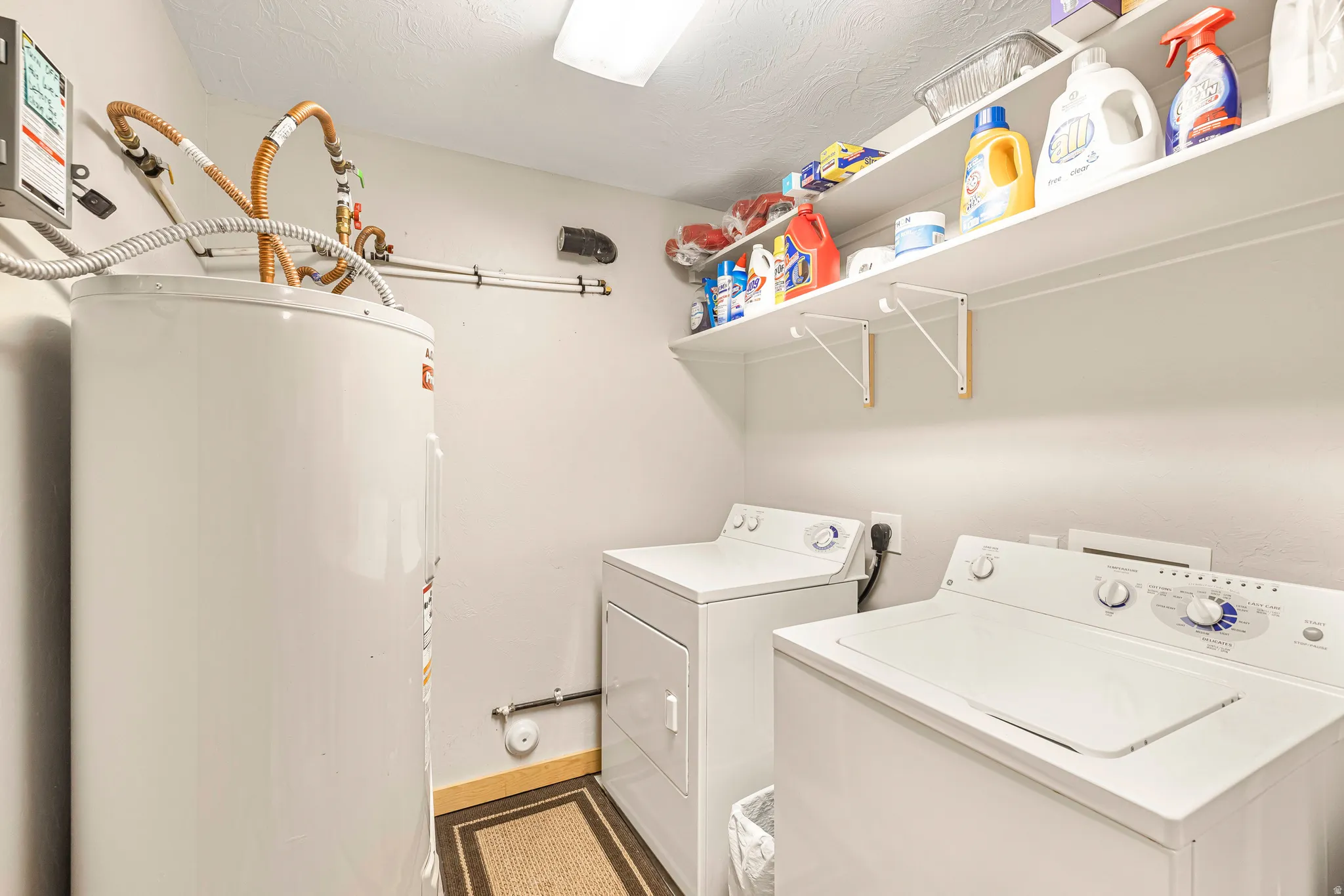 Laundry area with water heater, washing machine and clothes dryer, and a textured ceiling