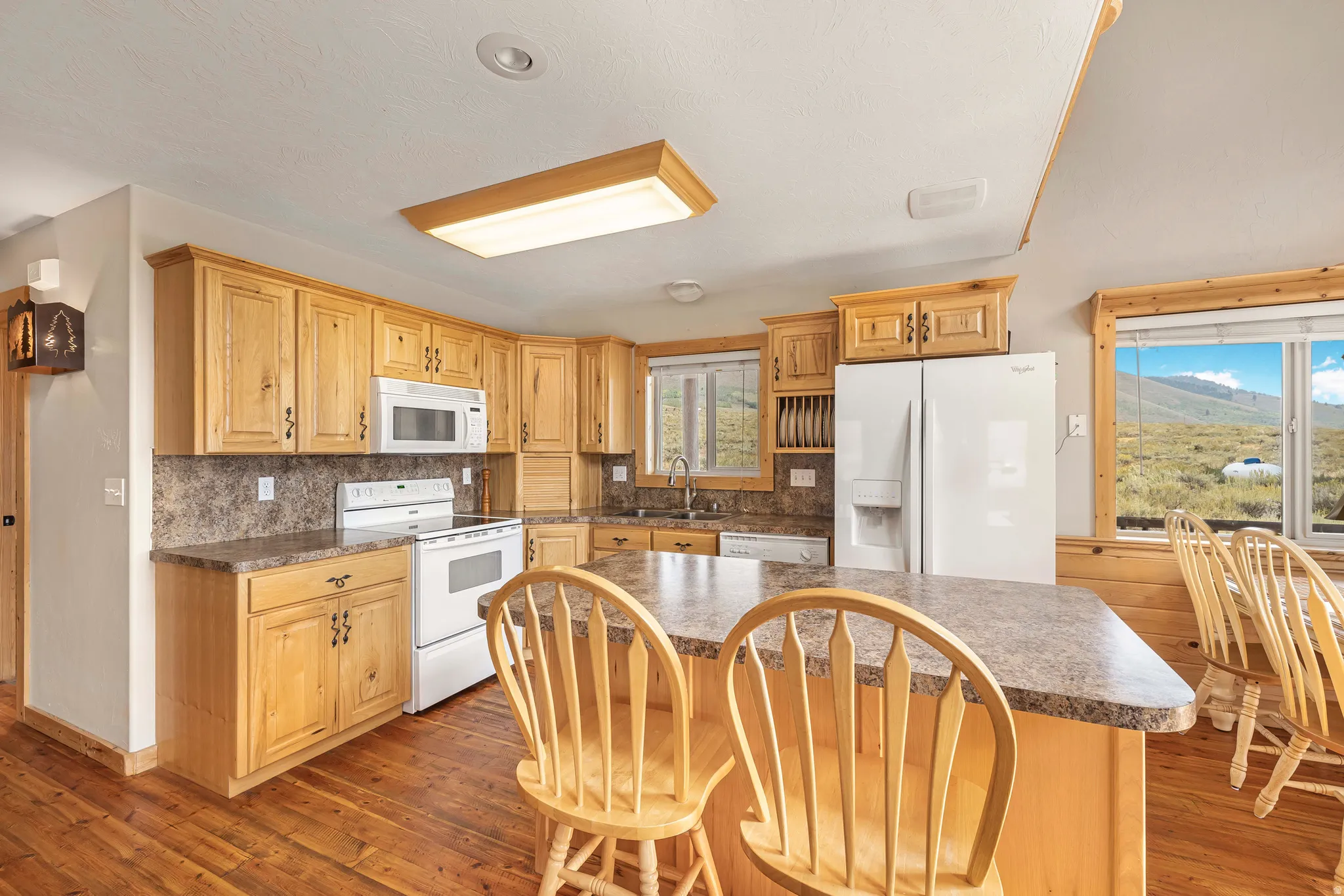 Kitchen with backsplash, white appliances, dark wood-style floors, dark countertops, and a kitchen bar