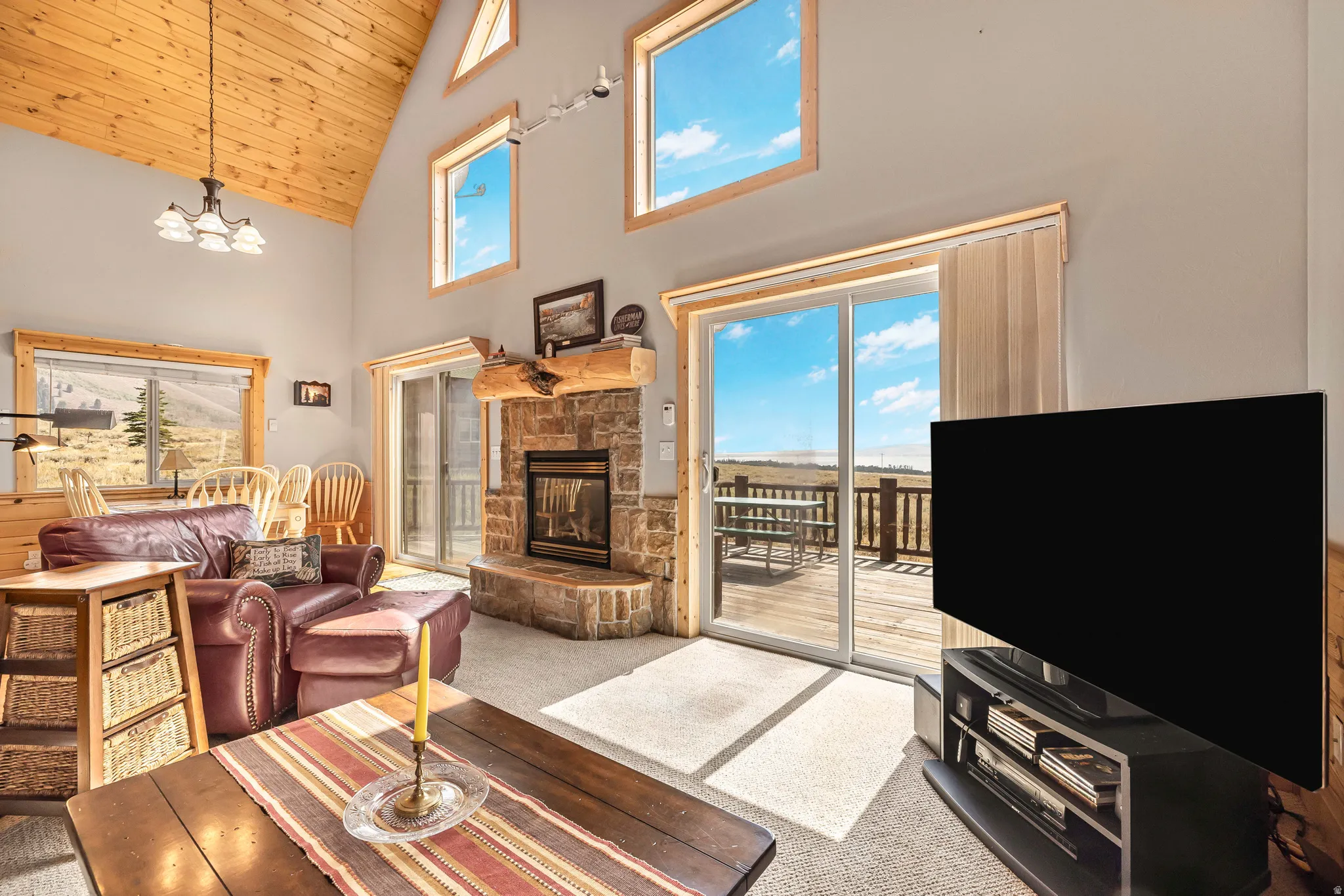 Carpeted living area with high vaulted ceiling, wooden ceiling, a fireplace, and a chandelier