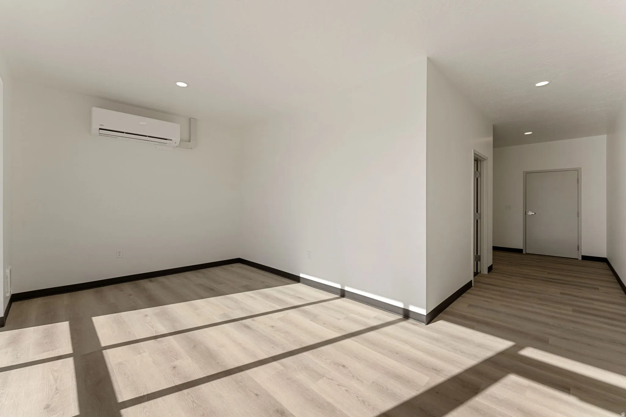 Empty room featuring light wood-style flooring, an AC wall unit, and recessed lighting