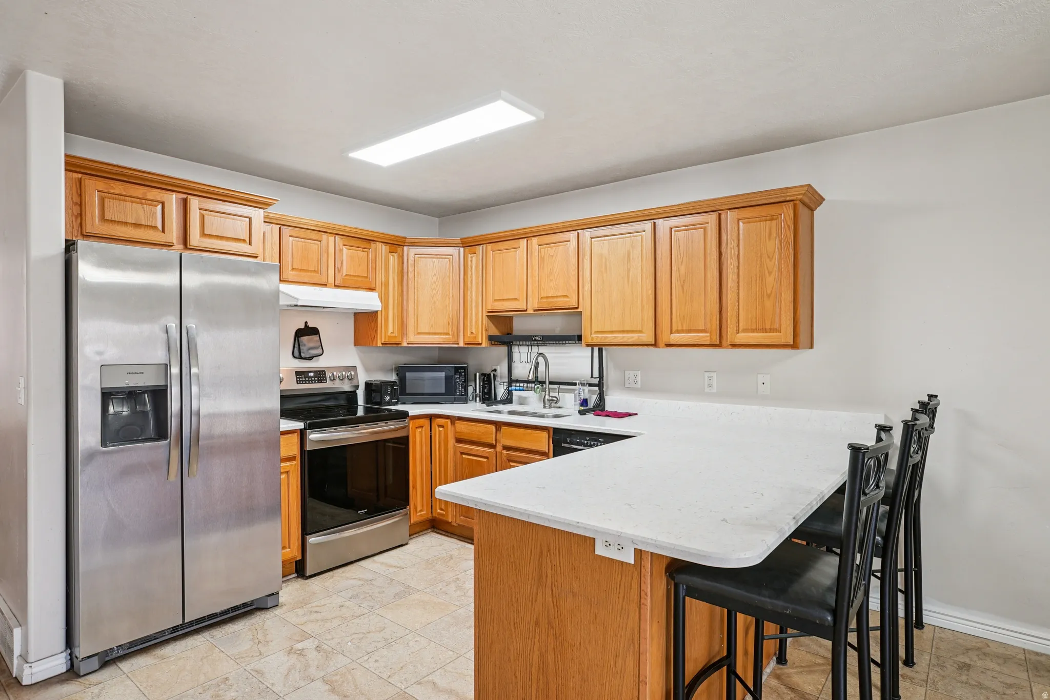 Kitchen featuring stainless steel appliances, a peninsula, a breakfast bar, under cabinet range hood, and light stone countertops