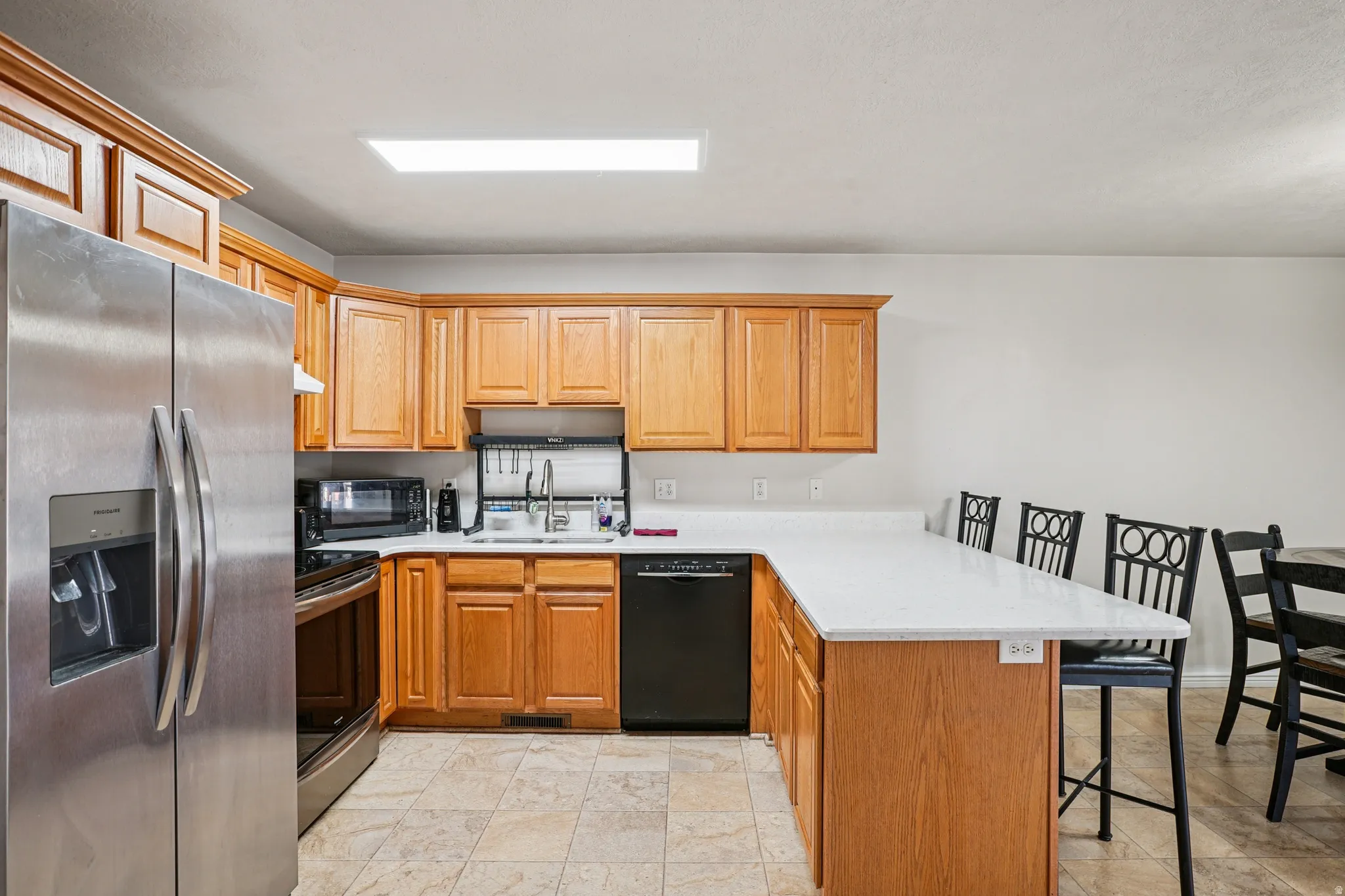 Kitchen with a breakfast bar area, a peninsula, black appliances, brown cabinetry, and light stone counters