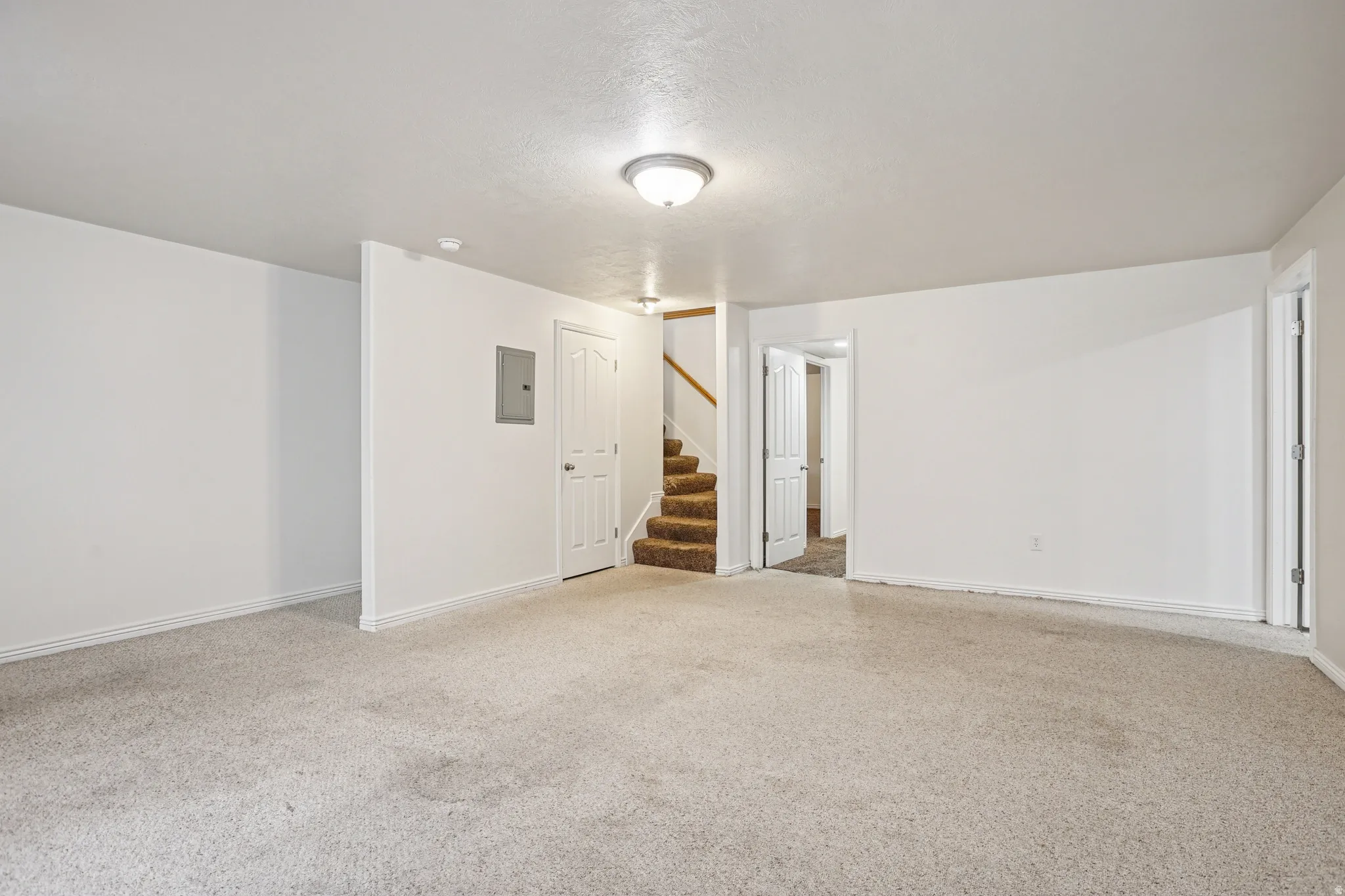 Spare room featuring light carpet, stairs, electric panel, and a textured ceiling