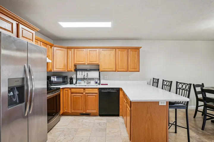 Kitchen with a breakfast bar area, a peninsula, black appliances, brown cabinetry, and light stone counters