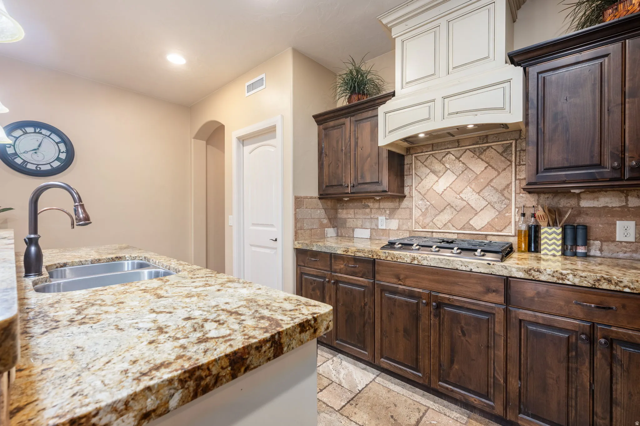Kitchen featuring dark brown cabinets, stone tile flooring, arched walkways, and recessed lighting