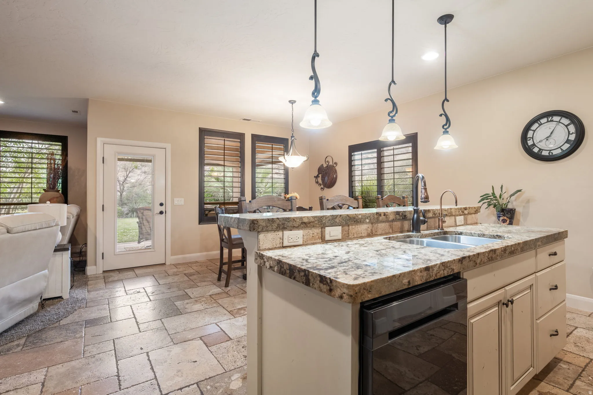 Kitchen with open floor plan, stone tile floors, a kitchen island with sink, dishwasher, and hanging light fixtures