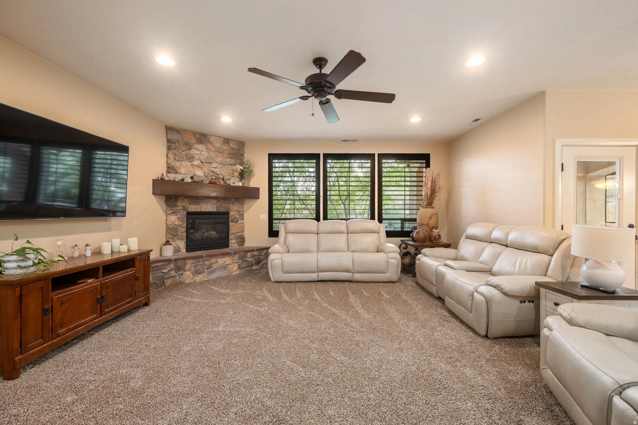 Living room featuring light colored carpet, a stone fireplace, ceiling fan, and recessed lighting