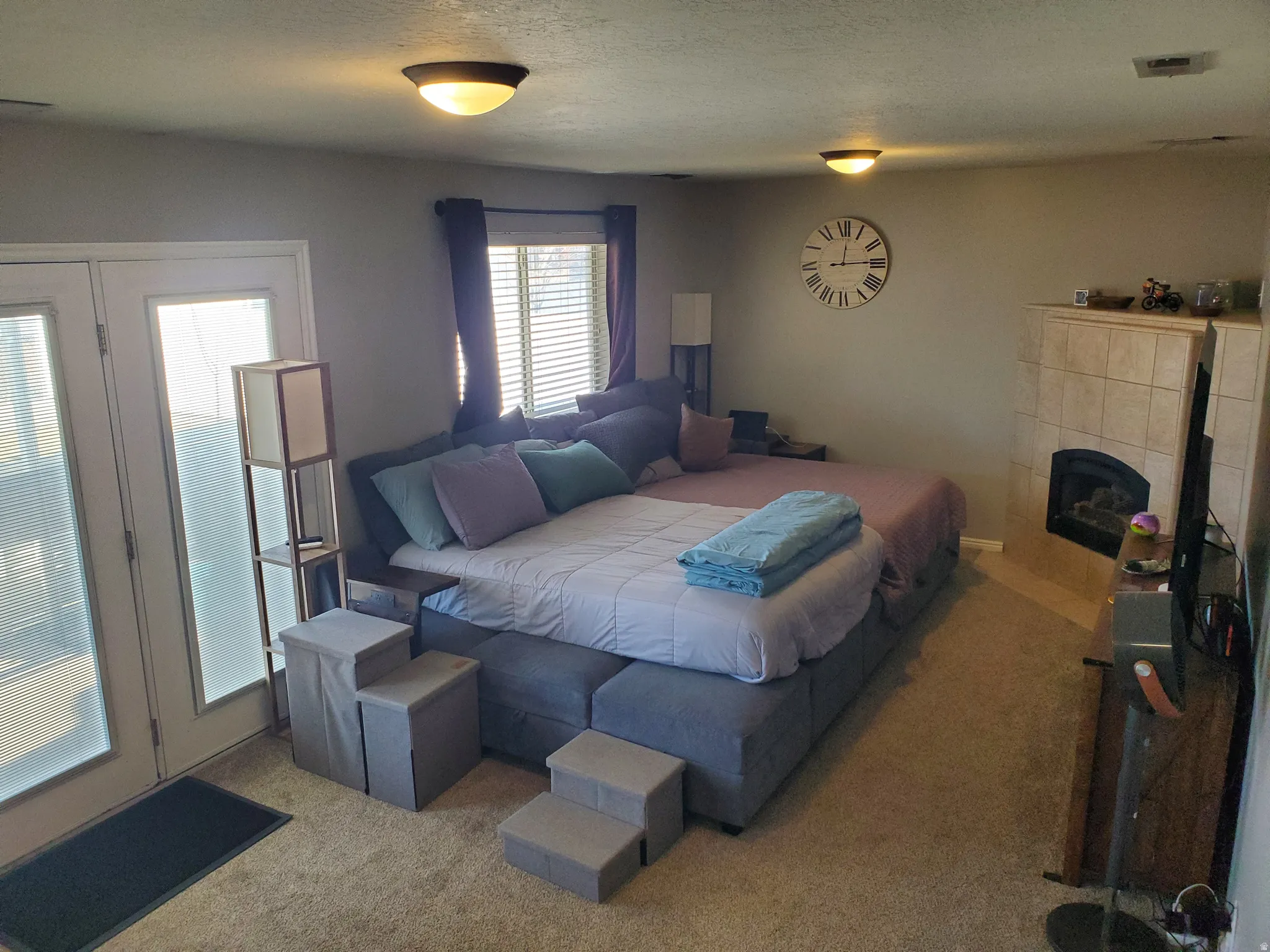 Carpeted bedroom featuring a tile fireplace, access to exterior, and a textured ceiling