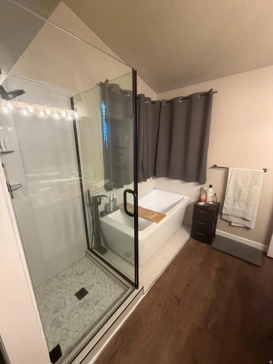Full bath featuring a shower stall, a garden tub, dark wood-style floors, and vaulted ceiling