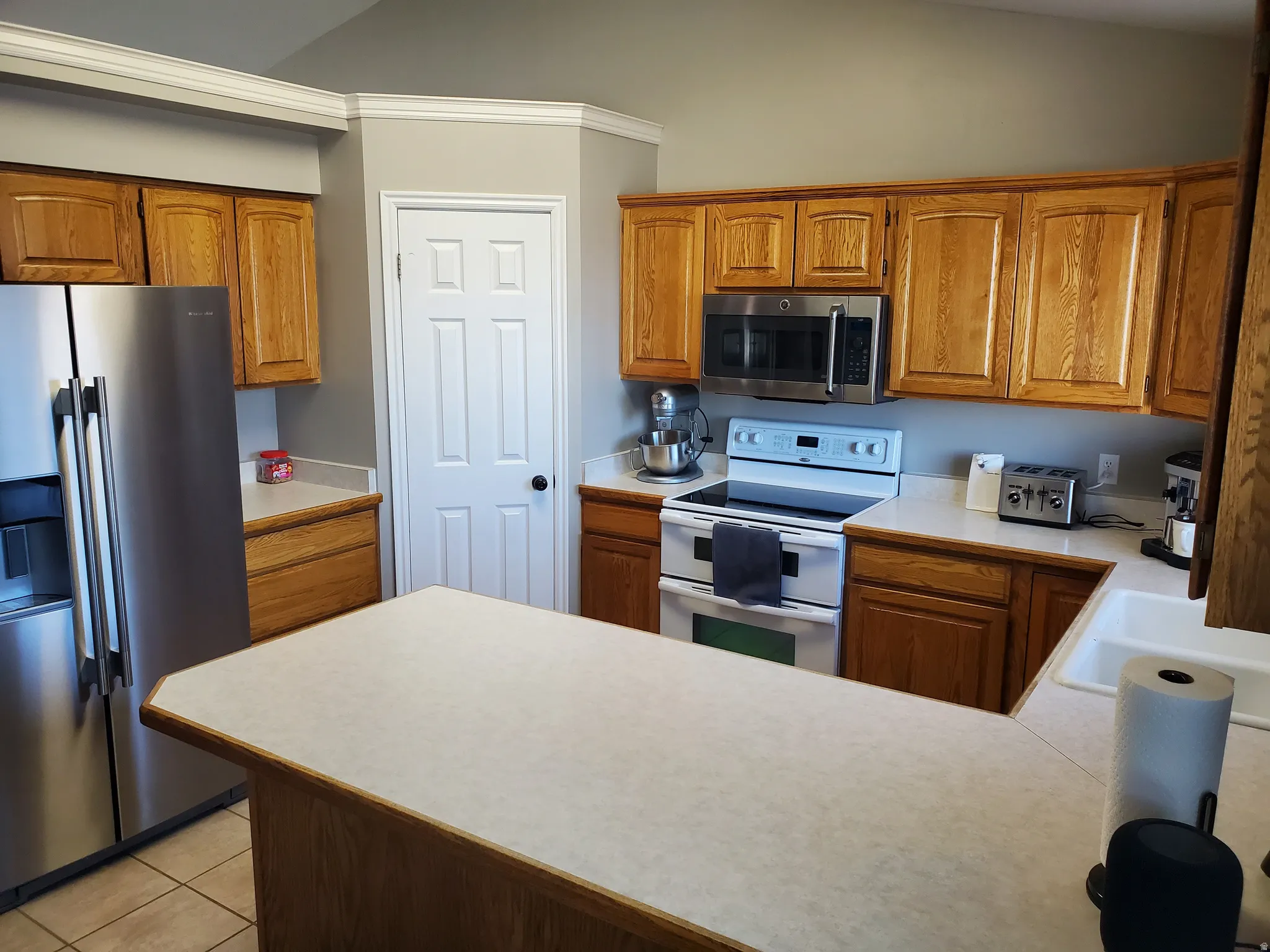 Kitchen featuring light countertops, stainless steel appliances, brown cabinets, and lofted ceiling