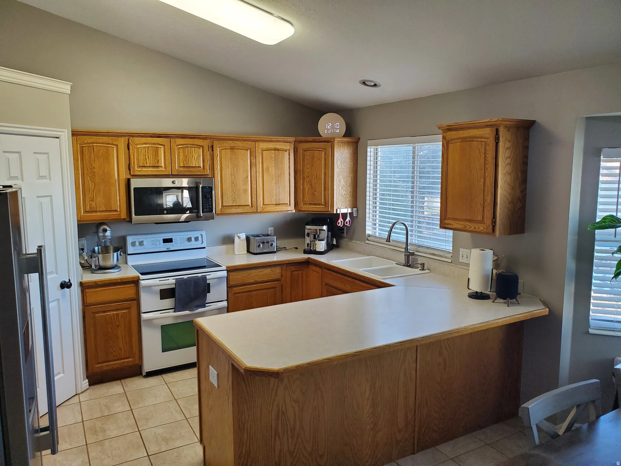 Kitchen featuring appliances with stainless steel finishes, light countertops, brown cabinets, vaulted ceiling, and a peninsula