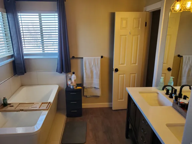 Full bath featuring a garden tub, double vanity, and dark wood-type flooring