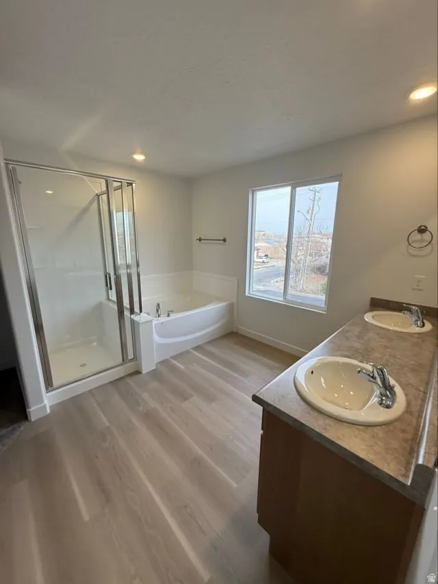 Bathroom featuring a garden tub, double vanity, a stall shower, light wood-style floors, and recessed lighting