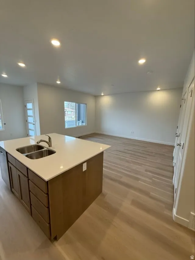 Kitchen with open floor plan, a center island with sink, light wood-style flooring, recessed lighting, and brown cabinetry
