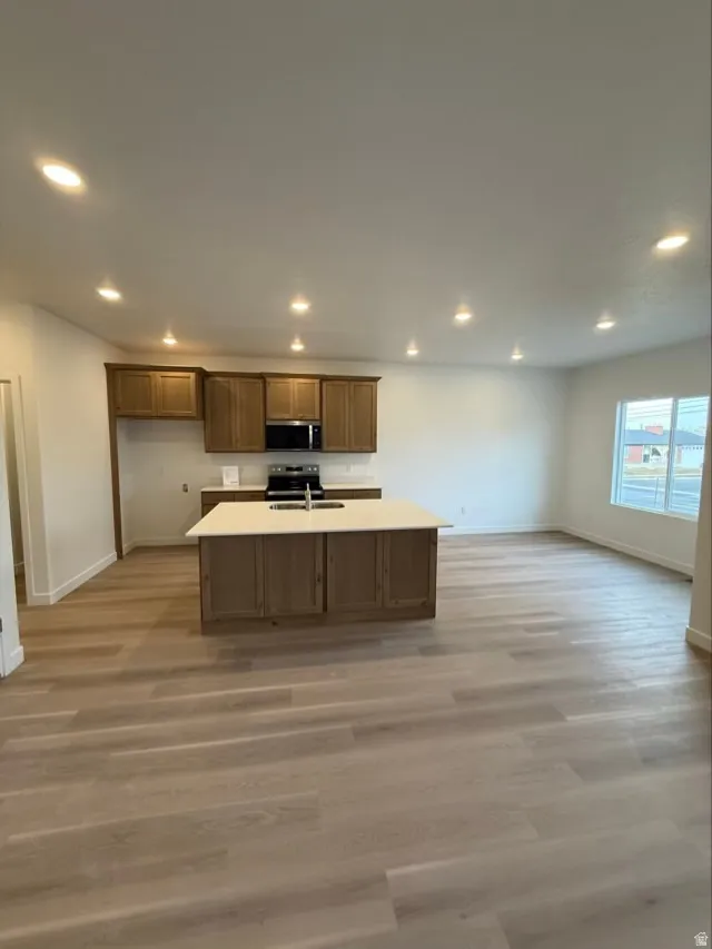 Kitchen with recessed lighting, light countertops, light wood-type flooring, stainless steel appliances, and brown cabinetry