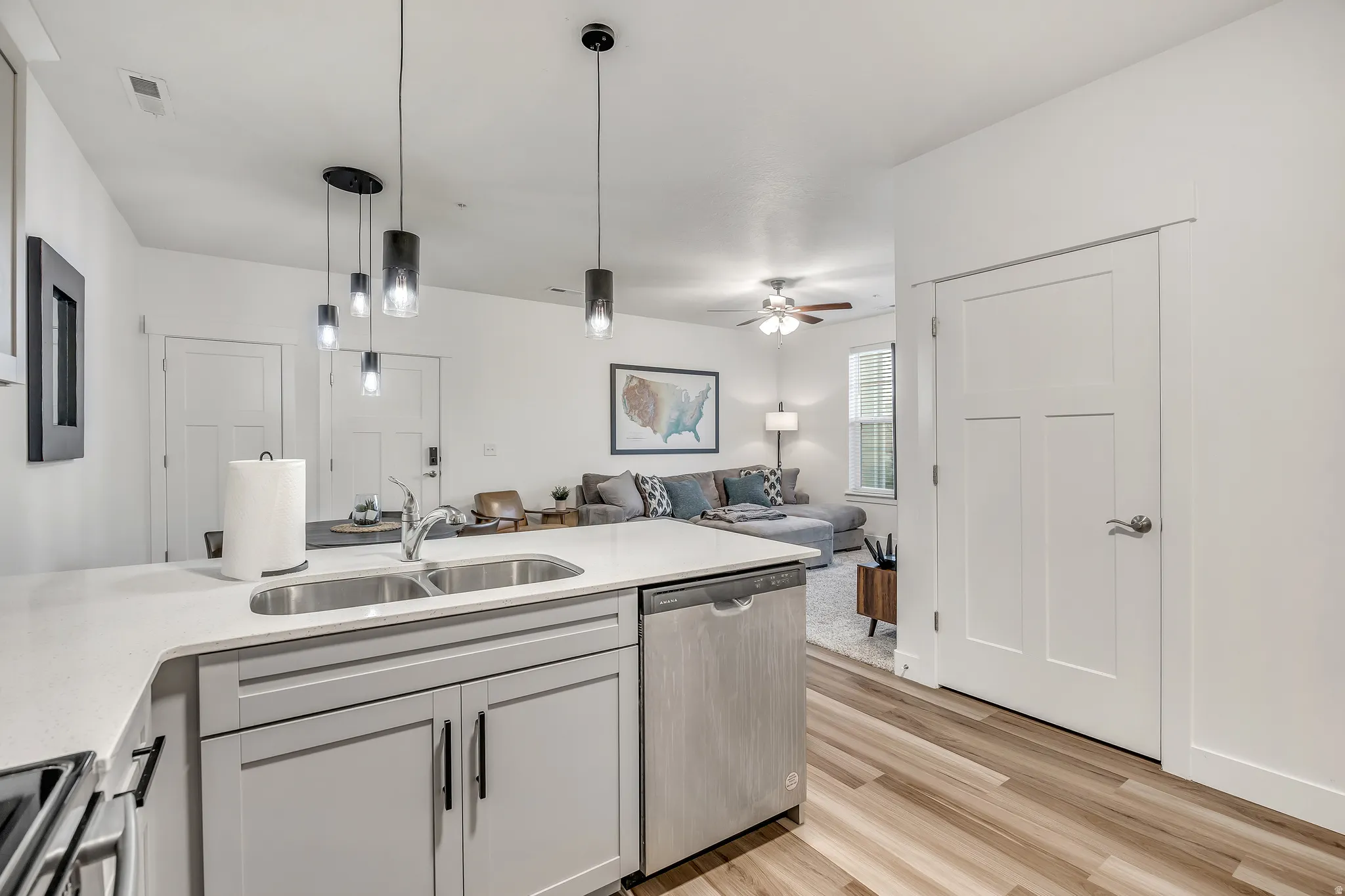 Kitchen with appliances with stainless steel finishes, decorative light fixtures, light wood-style floors, and light stone counters