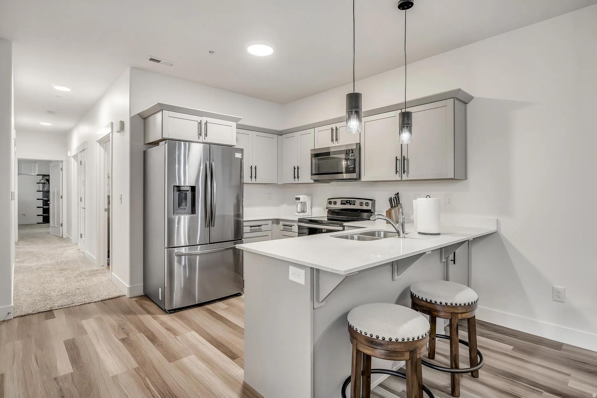 Kitchen featuring appliances with stainless steel finishes, a breakfast bar, light wood-type flooring, a peninsula, and recessed lighting