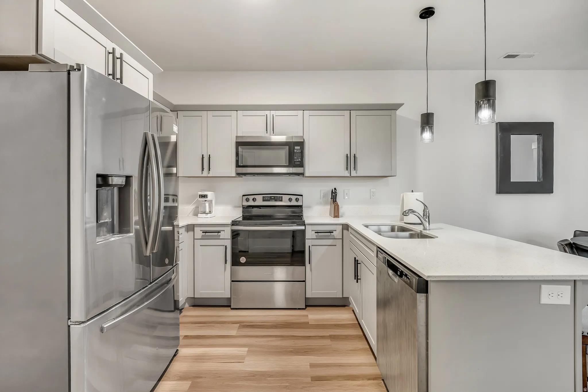Kitchen featuring appliances with stainless steel finishes, a peninsula, decorative light fixtures, light wood-type flooring, and light stone counters