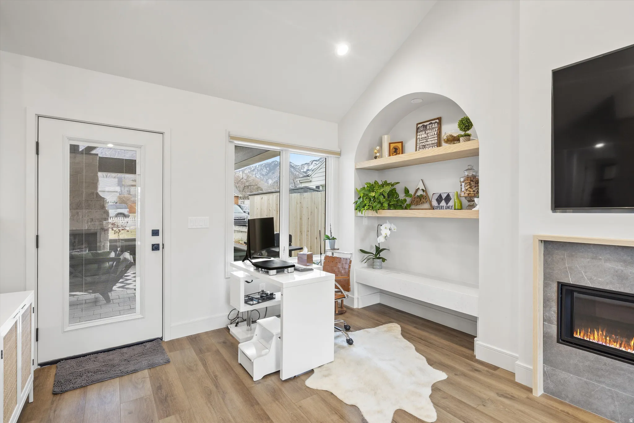 Vaulted ceiling, light wood-style flooring, a tiled fireplace, built in features, and recessed lighting