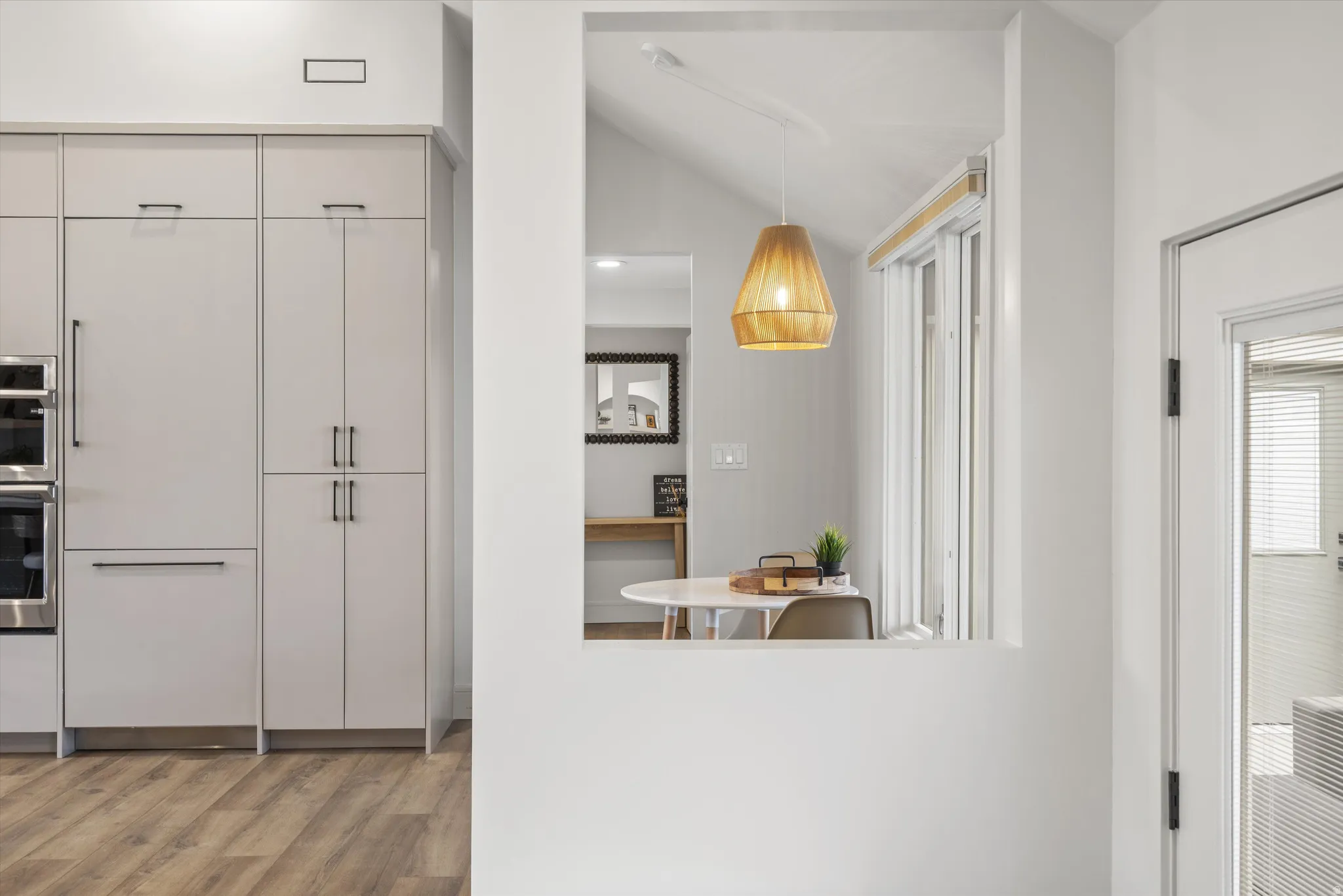 Kitchen with light wood-type flooring, pendant lighting, paneled fridge, stainless steel double oven, and lofted ceiling
