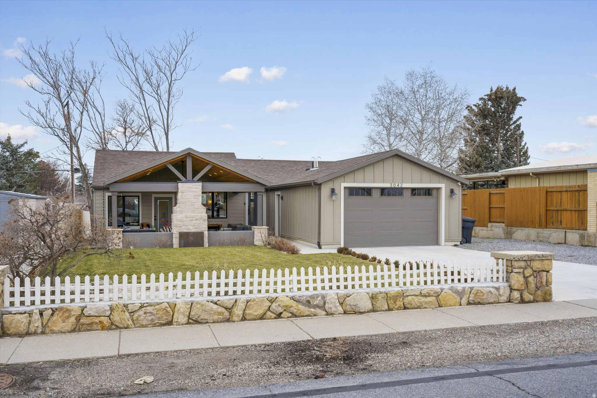 View of front facade featuring a fenced front yard, covered porch, a garage, board and batten siding, and driveway