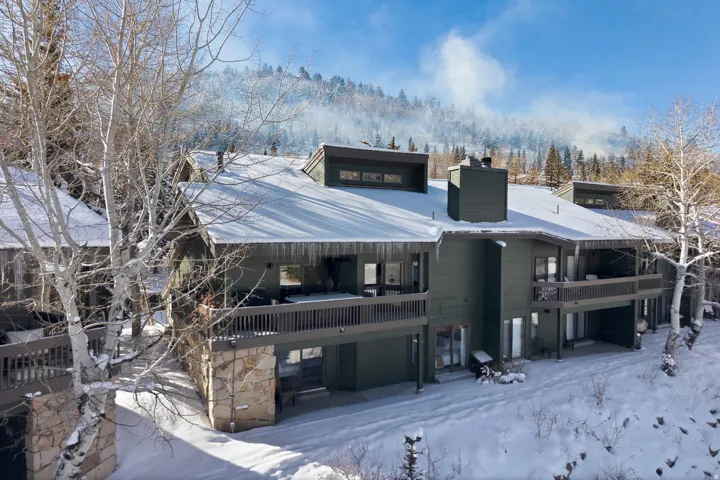 Snow covered house with a chimney, a patio area, stone siding, and a balcony