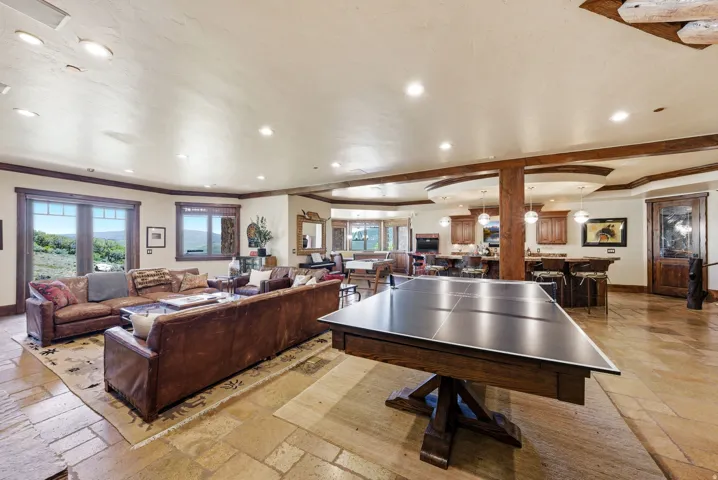 Spacious room featuring natural stone tile flooring, beamed ceilings, and recessed lighting