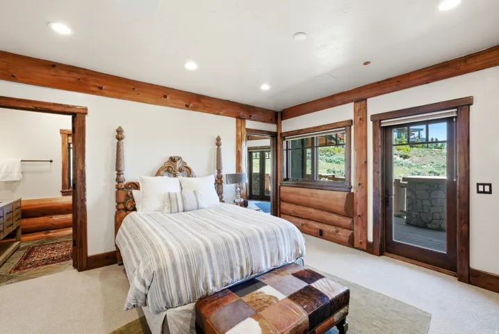 Expansive room featuring exposed wooden beams, recessed lighting, carpet flooring, and a glass-paneled door opening to an outdoor patio with a stone half-wall