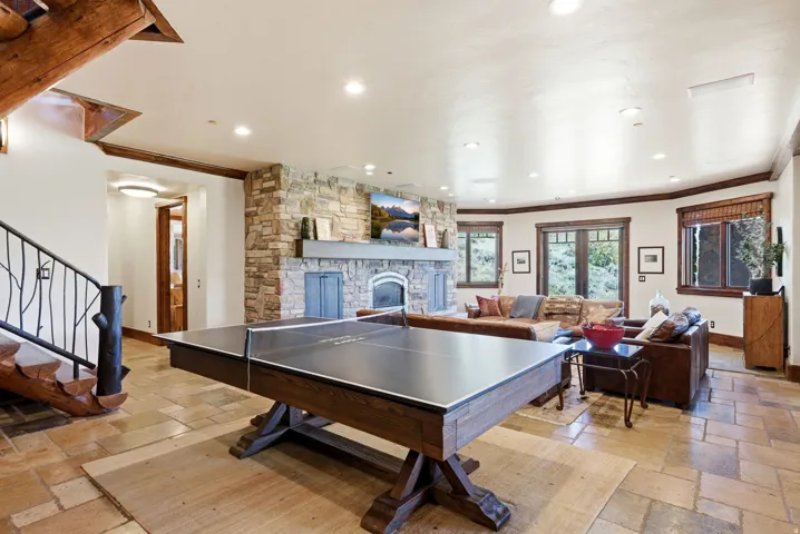 Spacious living area featuring stone-finish flooring, a prominent stone fireplace, recessed lighting, and large windows with dark wood trim