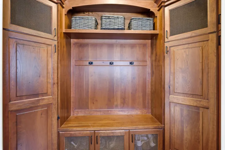 Built-in wood-finish cabinetry featuring a central bench, upper shelving, and lower storage with mesh-front doors