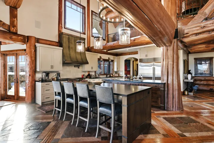 Open-concept kitchen featuring an oversized island with seating, stainless steel appliances, custom cabinetry, and a statement range hood