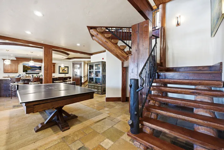 Warm-toned wood staircase with wrought iron railing, complemented by large format natural stone flooring