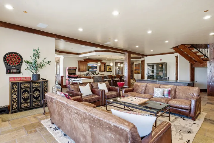 Open-concept living area featuring light-toned flooring, exposed wood beams, recessed lighting, and a built-in wet bar with a dark countertop
