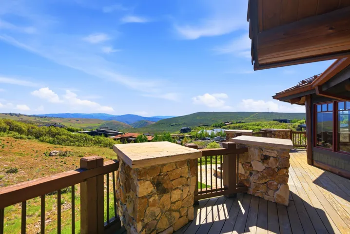 Expansive outdoor deck featuring wood-finish flooring and stone-clad pillars, overlooking rolling hills and distant properties
