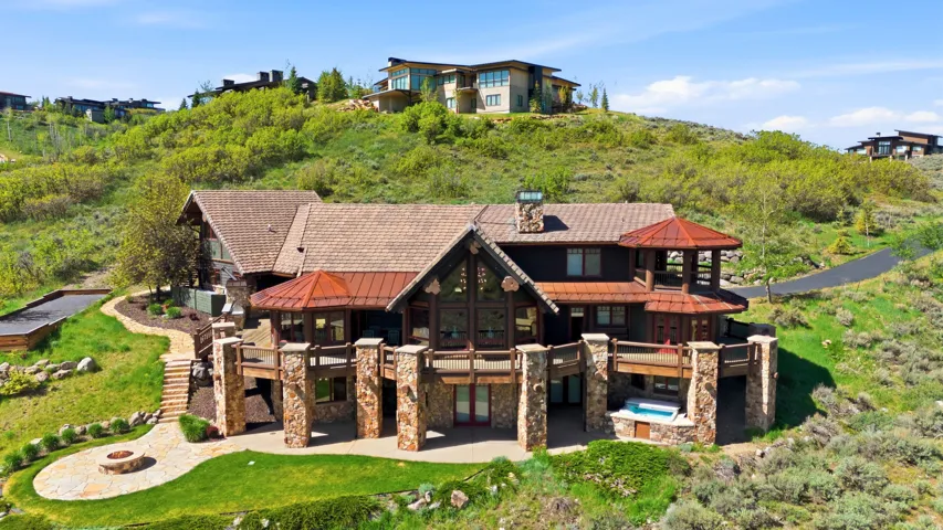 Multi-level residence featuring extensive stone work, a covered deck with integrated spa, and a stone fire pit area