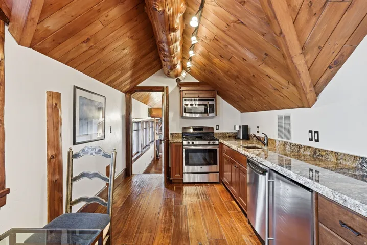 Kitchenette featuring wood-finish flooring, wood-paneled vaulted ceiling, stainless steel appliances, granite-style countertops, and rich wood cabinetry
