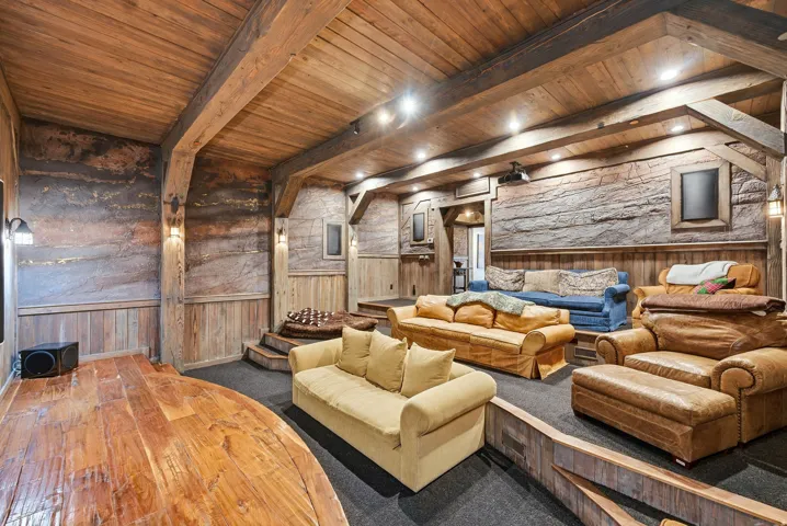 Entertainment room featuring tiered seating, wood-paneled walls with textured accents, exposed wood beams, and recessed lighting