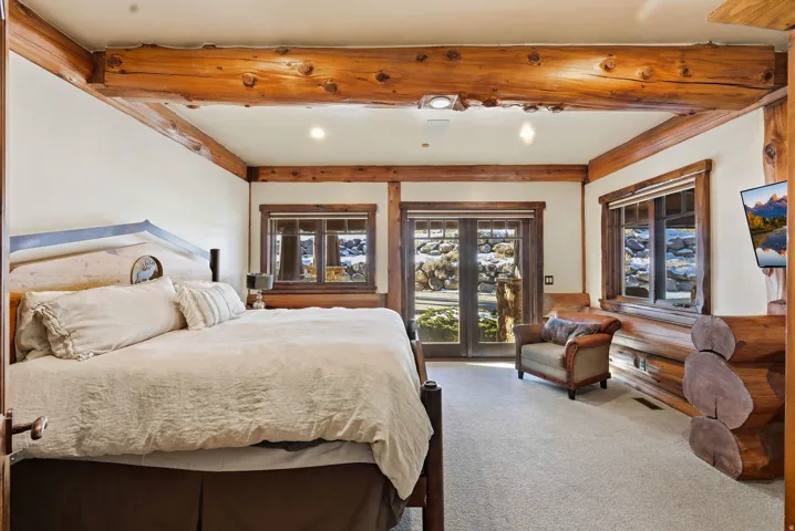 Bedroom featuring exposed wood beams, light-colored carpeting, and a double-door exterior access point