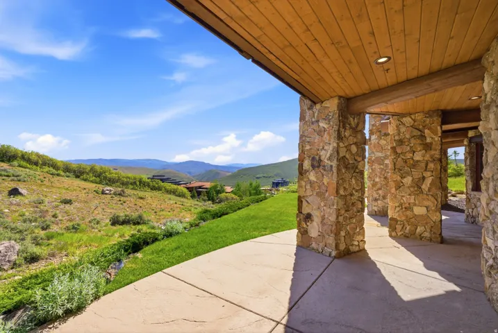 Covered patio with stone pillars and a wood-finish ceiling, overlooking a natural landscape with distant hills