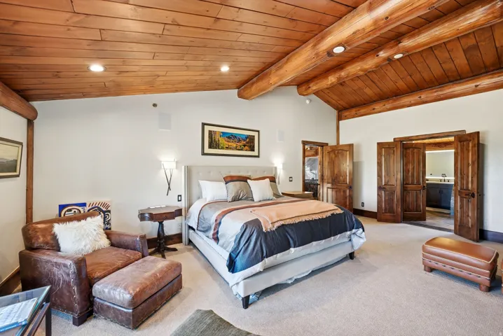 Spacious room featuring a vaulted wood-plank ceiling with exposed log beams, recessed lighting, and wall-mounted sconces