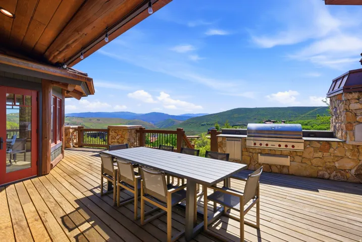 Expansive outdoor deck featuring wood-finish flooring, a built-in stone outdoor kitchen with a stainless steel grill, and a wood-paneled ceiling with track lighting