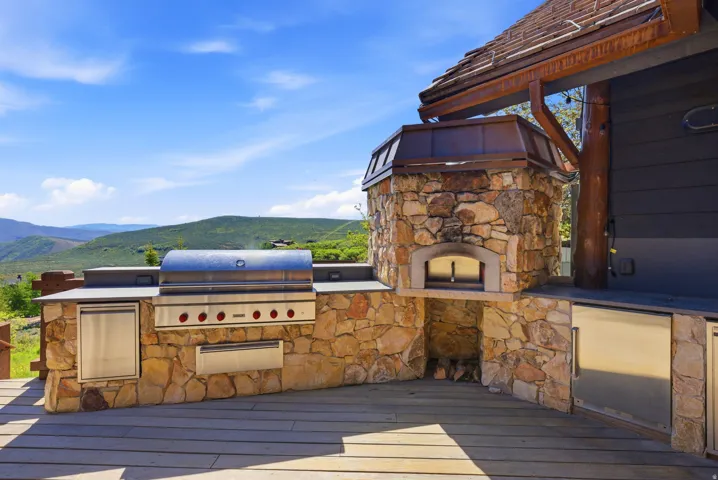 Outdoor kitchen featuring stone construction, built-in grill, integrated outdoor refrigerator, and a pizza oven with a copper hood