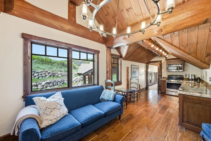 Open-concept living space featuring wood-finish flooring, exposed wood beam ceiling, and a large window overlooking a rock garden