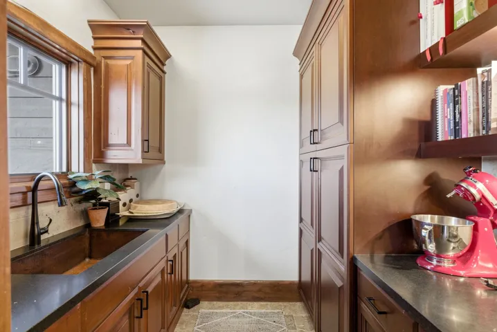 Custom wood cabinetry with black hardware, a window-framed copper sink, and dark countertops