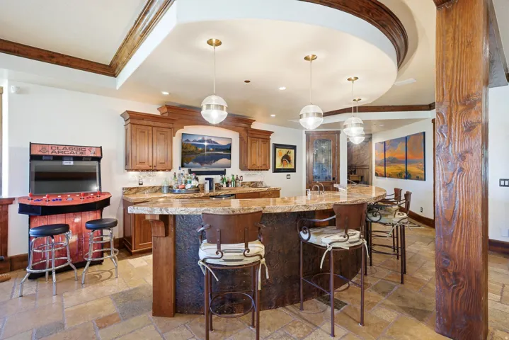 Entertainment space featuring a curved bar with stone-finish countertop, wood cabinetry, and three pendant lights
