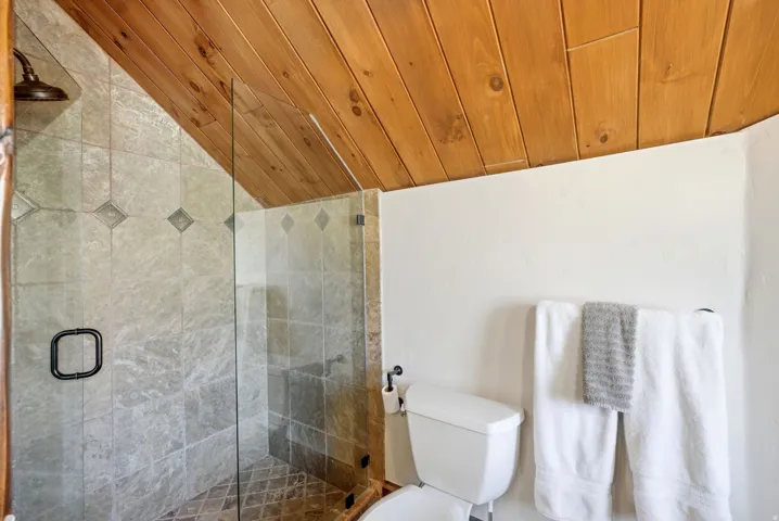 Shower enclosure featuring full height glass panels, a dark bronze shower head, and gray stone-finish tile with decorative diamond accents