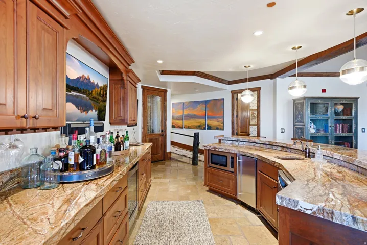 Spacious entertainment area featuring rich wood cabinetry, natural stone countertops, recessed lighting, integrated appliances, and spherical pendant light fixtures